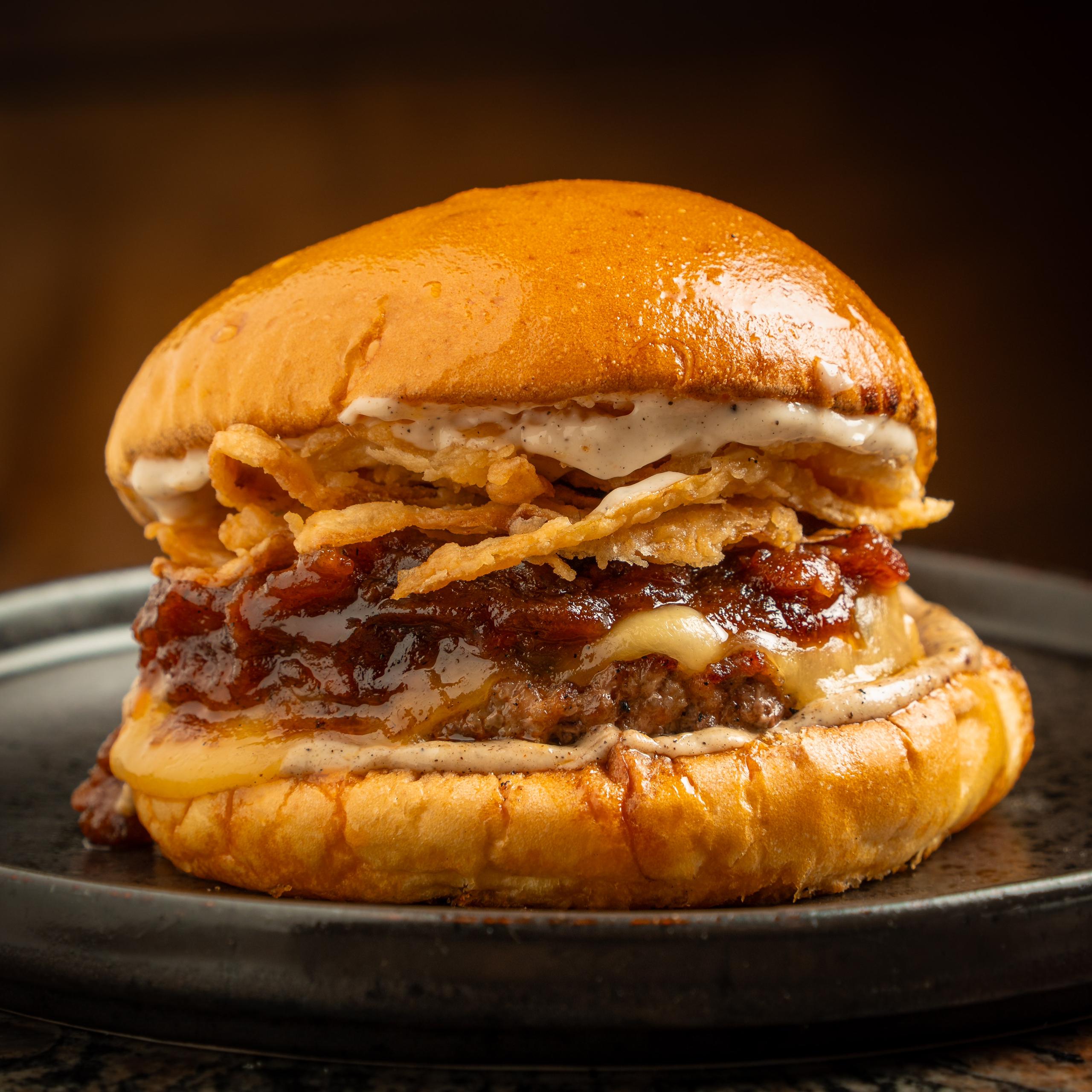 Pan brioche de mantequilla artesanal, 200 grs de nuestro jugosa carne al carbón, queso holandés, mermelada de tocineta en maple y Ron, cebollas crispy y mayo trufada, no incluyen papas